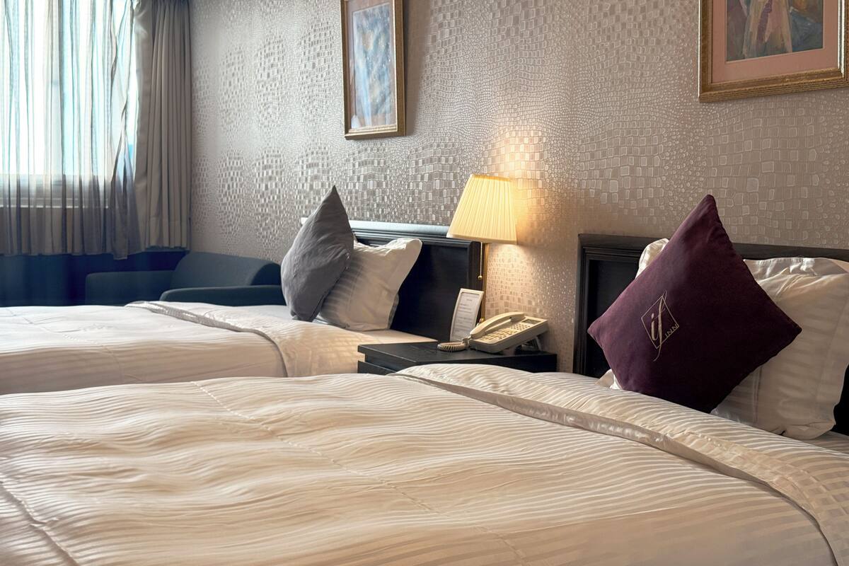 A hotel room with two beds, a nightstand with a lamp, a telephone, and a painting on the wall.