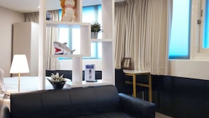 Una sala de estar moderna con un sofá negro, una mesa de centro de vidrio y un estante blanco con objetos decorativos.