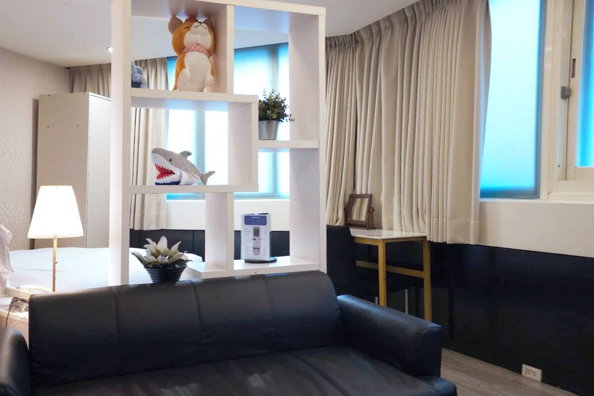 A modern living room with a black sofa, glass coffee table, and a white shelving unit with decorative items.
