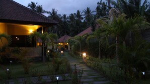 A pathway leading to a building with a tiled roof, surrounded by palm trees and well-maintained gardens. - ArcoIris (Karangasem)