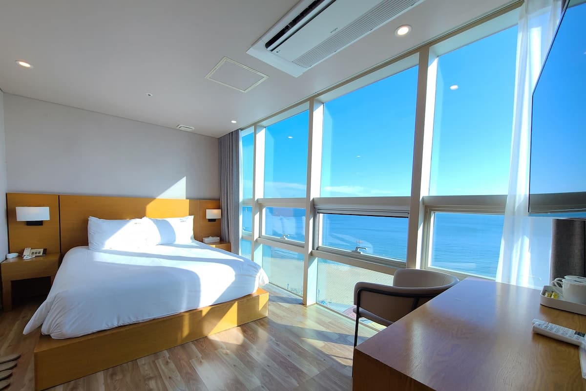 A hotel room with a large bed, a desk, and a view of the sea.