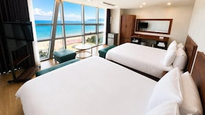 Ein Hotelzimmer mit zwei Betten, einem Fernseher, einem Schreibtisch und Blick auf den Strand.