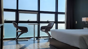 Ein Hotelzimmer mit großem Fenster, einem Bett, zwei Sesseln und einem kleinen Tisch.