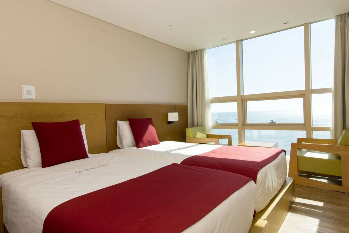 A hotel room with two beds, a large window, and a view of the sea.