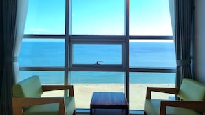 Ein Zimmer mit großen Fenstern und Meerblick. Zwei Stühle und ein kleiner Tisch stehen im Raum.
