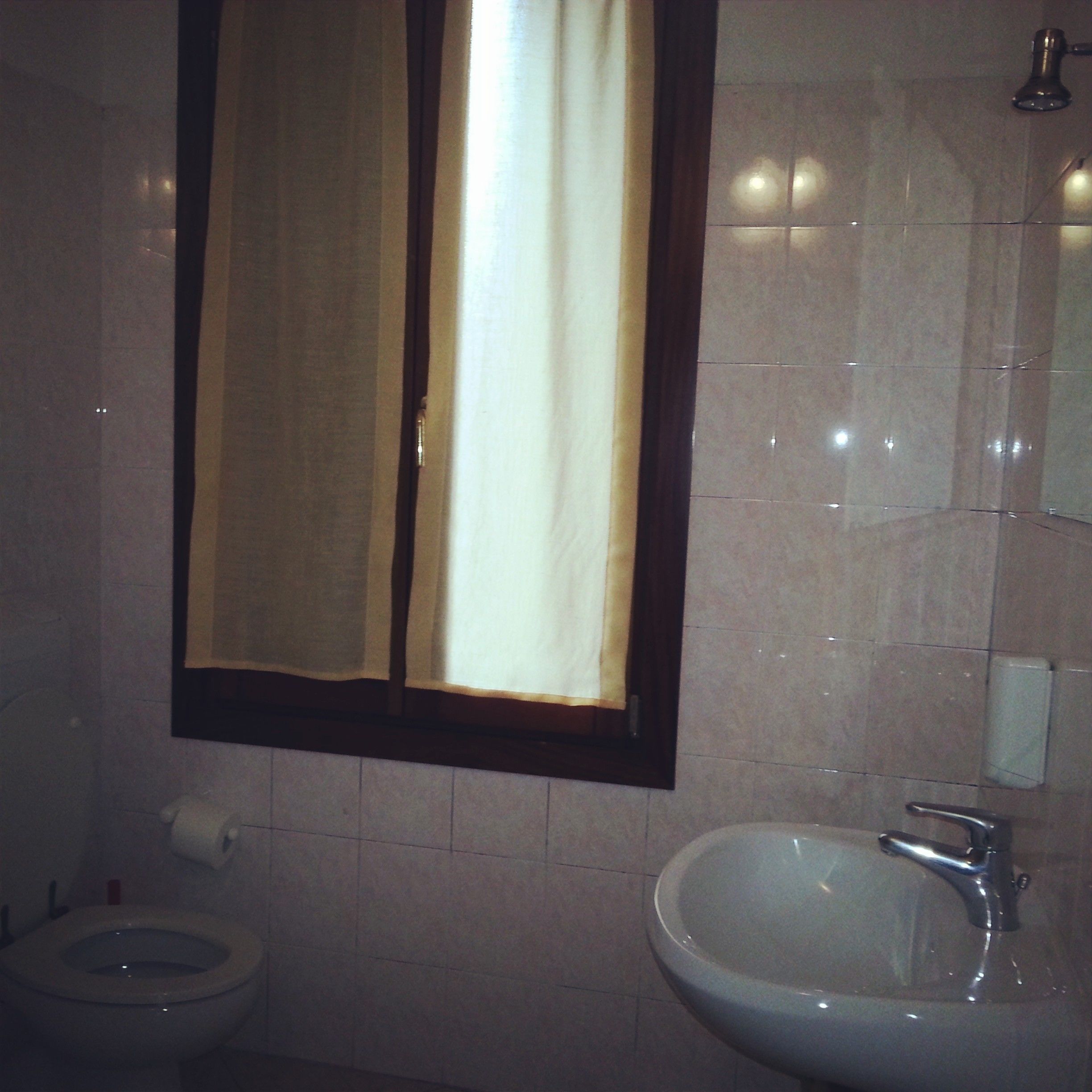 Une salle de bain comprenant des toilettes, un lavabo et un miroir, avec une fenêtre située au-dessus.