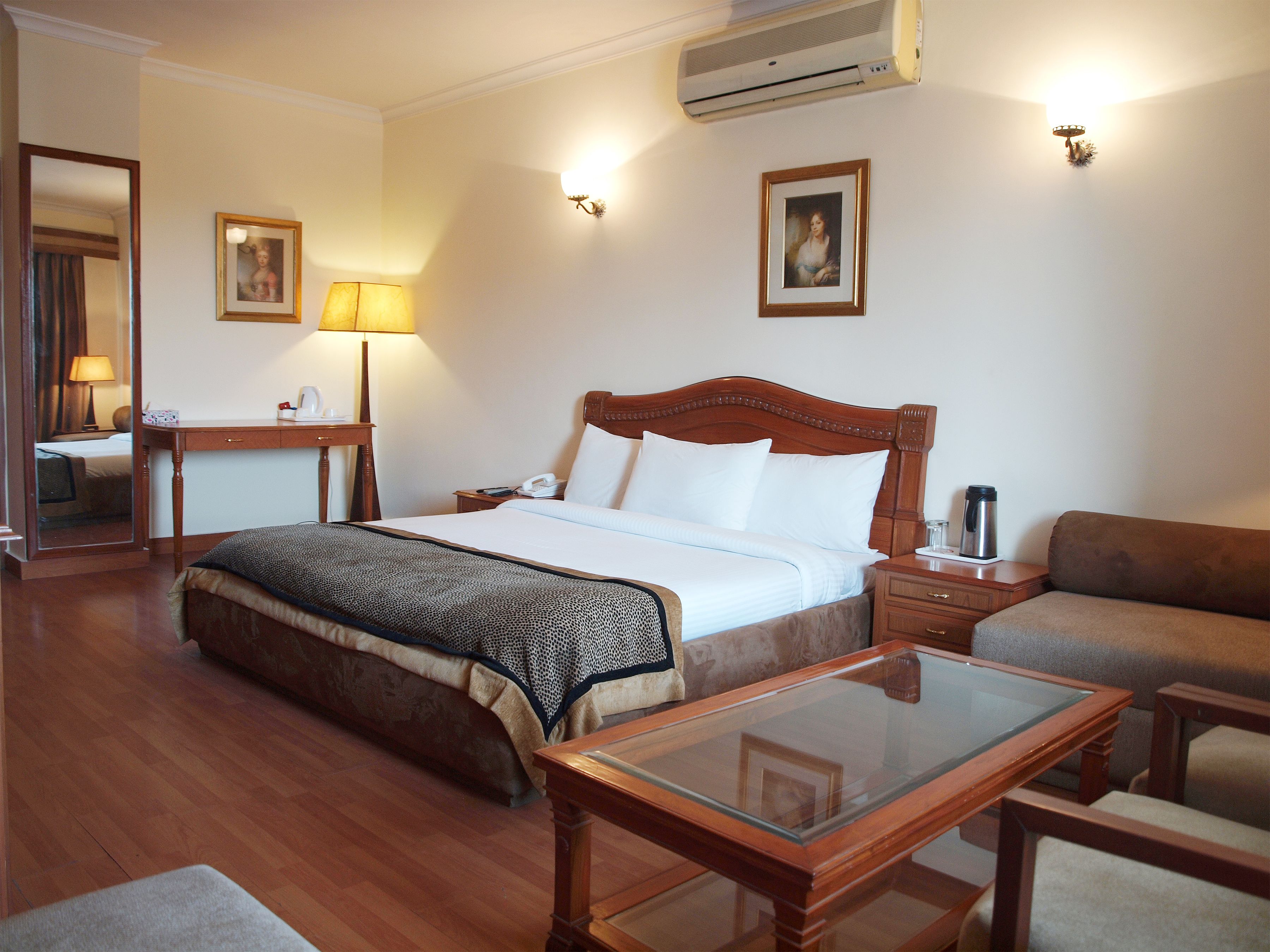 A hotel room with a bed, bedside table, lamp, and a glass-top table.