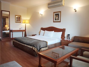 A hotel room with a bed, bedside table, lamp, and a glass-top table. - The BMK Hotel  (New Delhi)