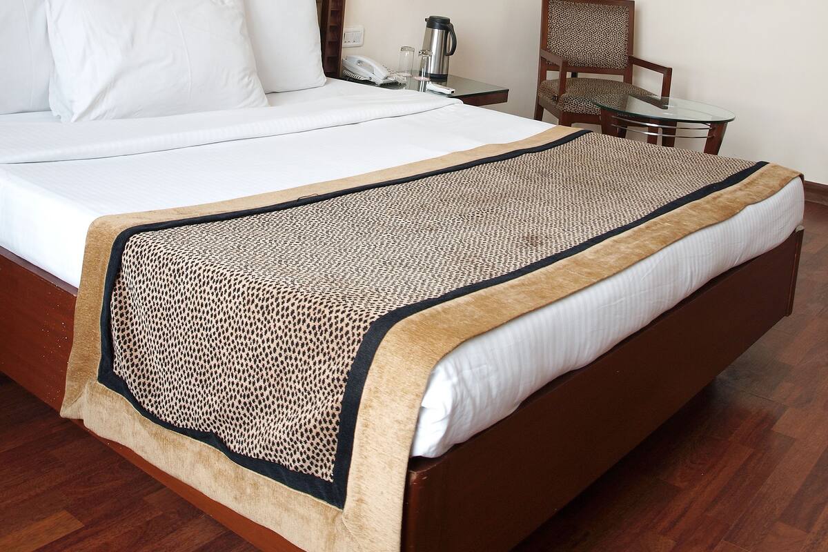 A hotel room with a large bed, a headboard with lights, a framed photo, a bedside table with a lamp, and a chair.