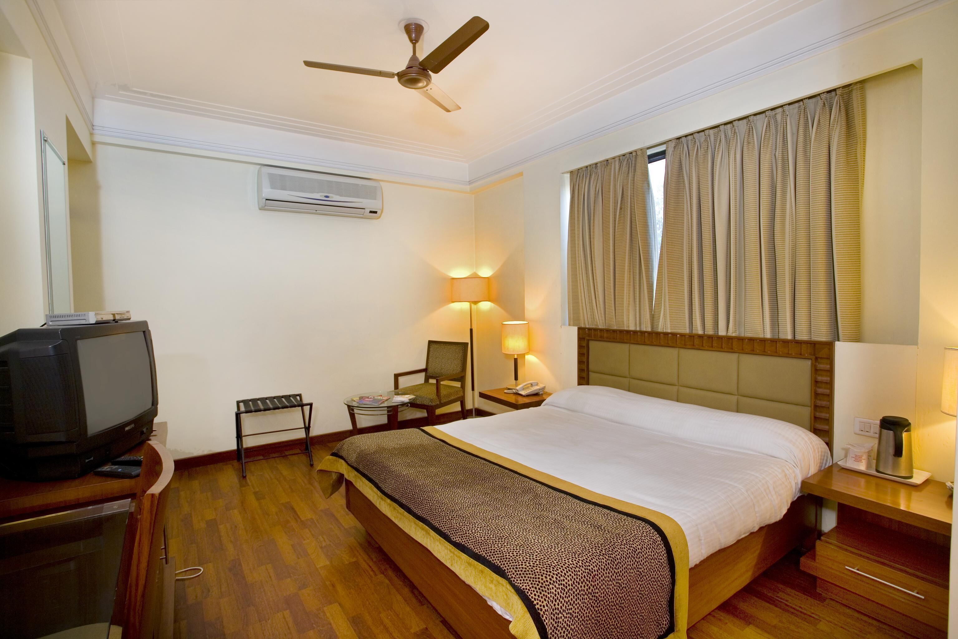 Een hotelkamer met een bed, een televisie, een bureau, een stoel, een lamp en een airconditioning.