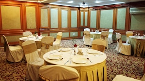 Un salón de banquetes con mesas redondas, sillas con lazos dorados y una alfombra estampada.