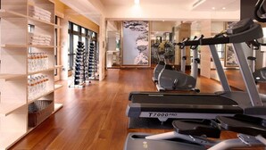 Un gimnasio moderno con cintas de correr, bicicletas estáticas y una pared decorada con un mural de paisaje montañoso.