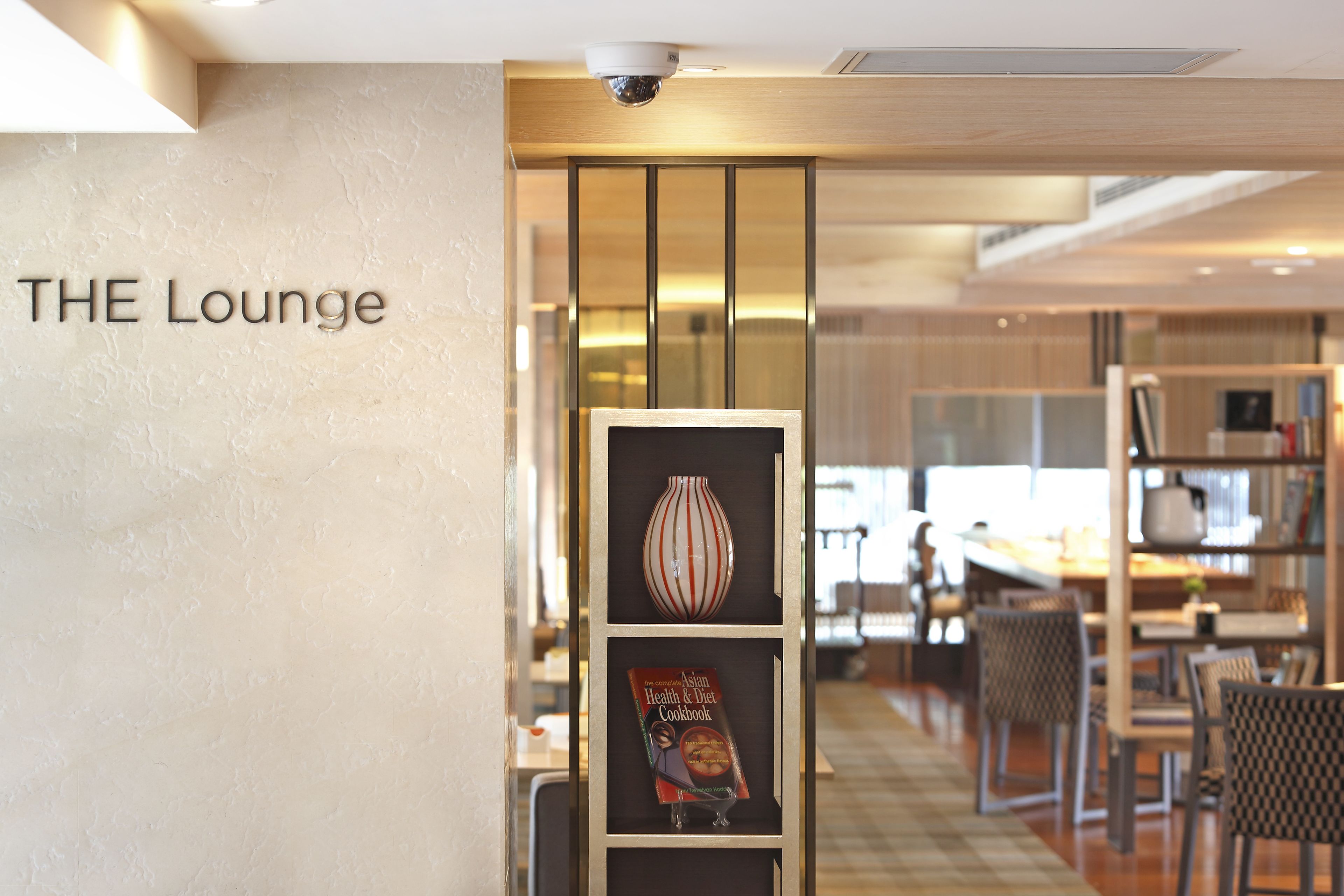 A modern lounge area with a sign reading "THE Lounge" and a display shelf with a book titled "Asian Health & Diet Cookbook".