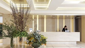 Un área de recepción moderna con una recepcionista en el mostrador, un jarrón grande con follaje y un diseño limpio y minimalista.