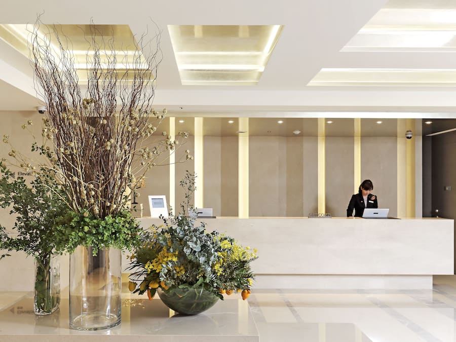A modern reception area with a receptionist at the desk, a large vase with greenery, and a clean, minimalist design.