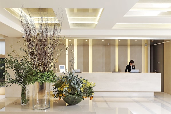 A modern reception area with a receptionist at the desk, a large vase with greenery, and a clean, minimalist design.