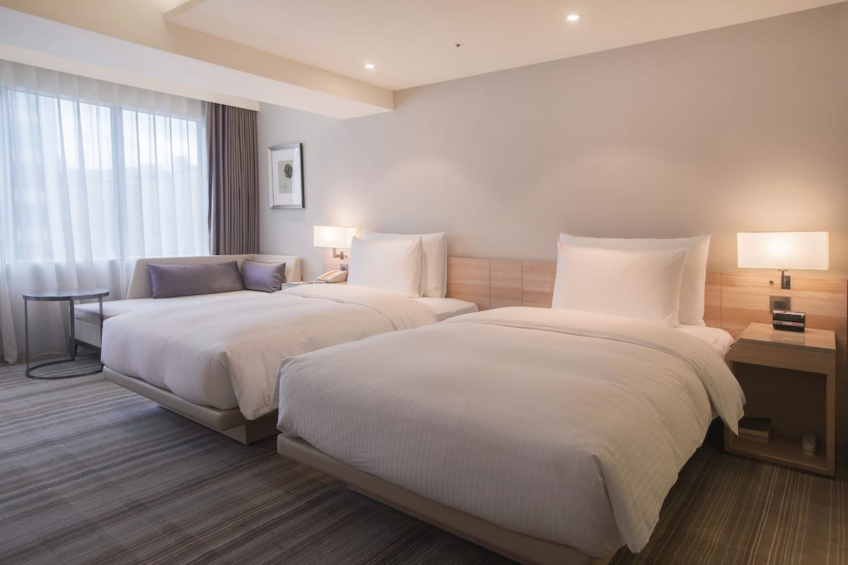 Habitación de hotel con dos camas, una mesita y una lámpara.