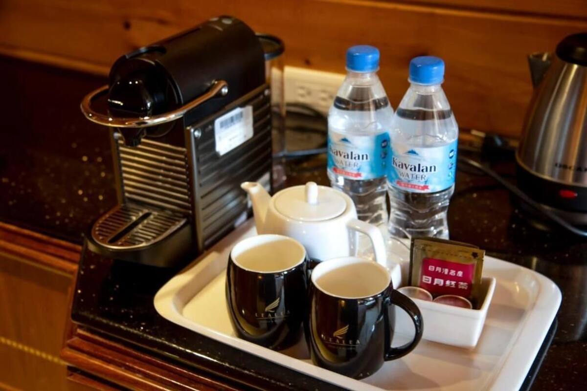 A tray with a coffee maker, two bottles of water, a teapot, two mugs, and a box of tea.
