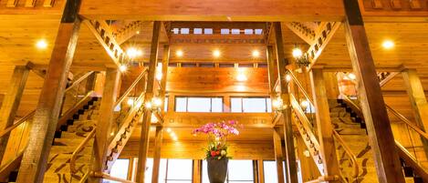 A spacious lobby with a high ceiling, wooden beams, a central staircase, and a large window offering a view.
