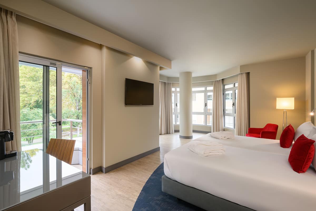 A hotel room with a large bed, a desk, a chair, and a TV on the wall.