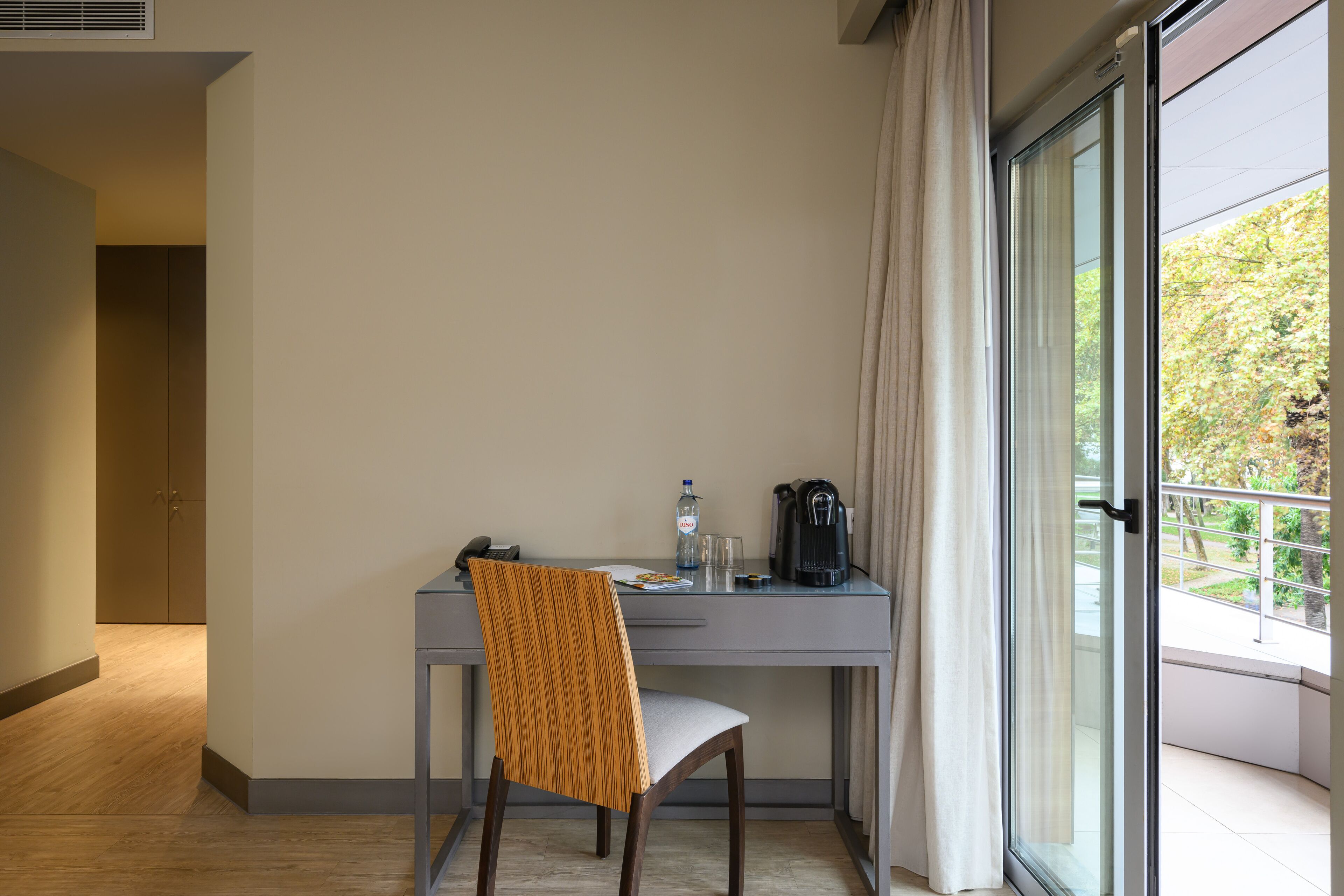 A hotel room with a desk, chair, and a large window with curtains.