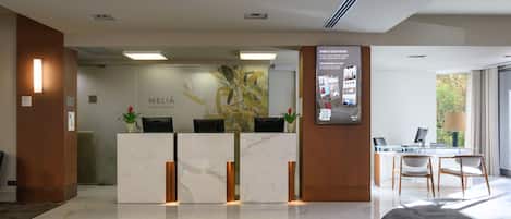 A hotel reception area with marble counters, a reception desk, and a seating area with chairs and a table.