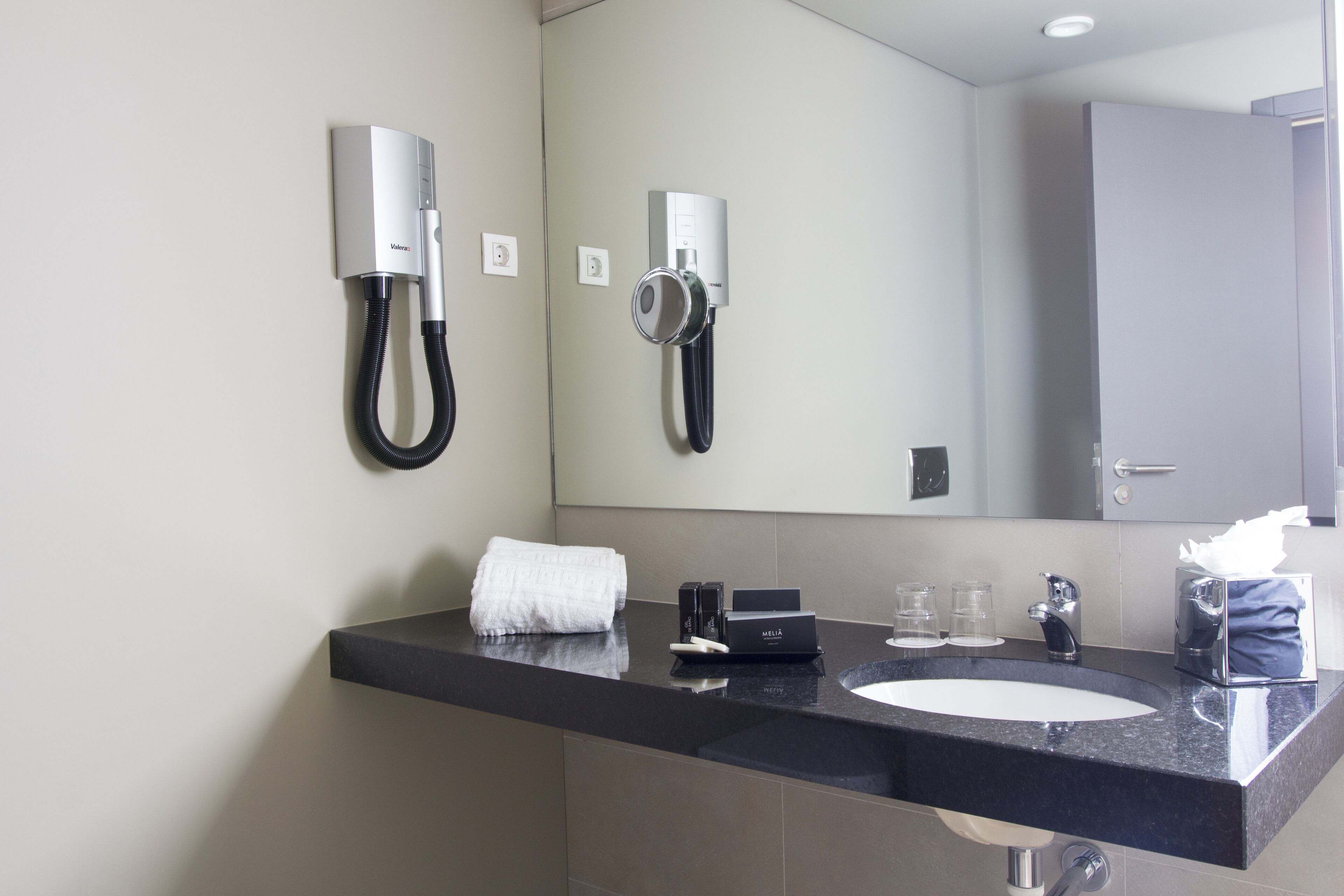 A modern bathroom with a black countertop, a white sink, a towel, a tissue box, and two mounted phones.