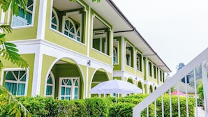 Un edificio de dos pisos con paredes exteriores verdes y blancas, múltiples ventanas y una escalera blanca que conduce a la entrada.