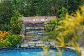 Une enseigne indiquant l’emplacement du Baan Suan Resort, avec un mur de pierre et une piscine au premier plan.
