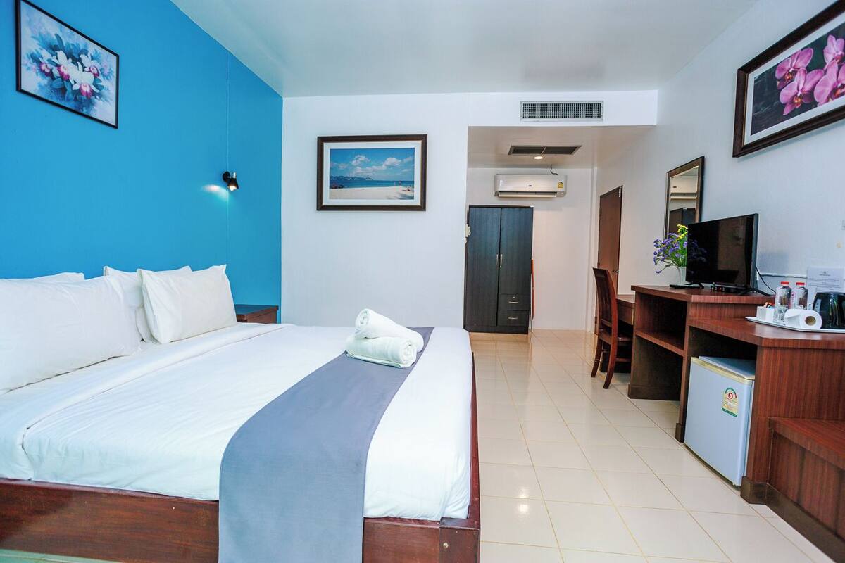 A hotel room with a bed, a desk with a computer, a TV, and a small fridge.