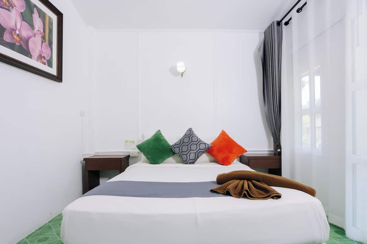 A hotel room with a bed, a nightstand, a lamp, and a window with curtains.