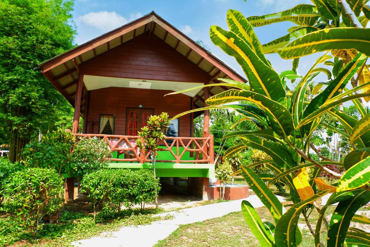 A wooden house with a porch, surrounded by lush greenery.