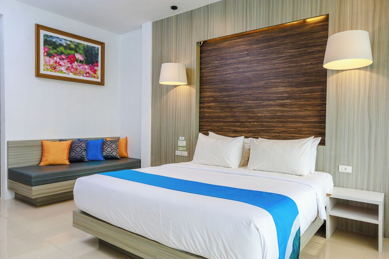 A modern hotel room with a large bed, a sofa, and two wall-mounted lamps.