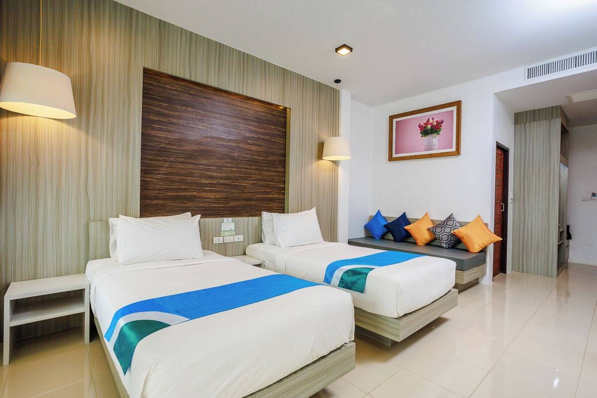 A hotel room with two beds, a sofa, and a large wooden panel on the wall.