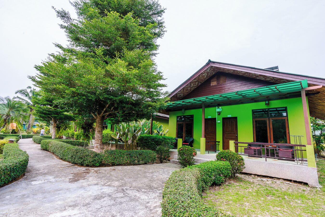 A green building with a covered porch, surrounded by well-maintained hedges and trees.