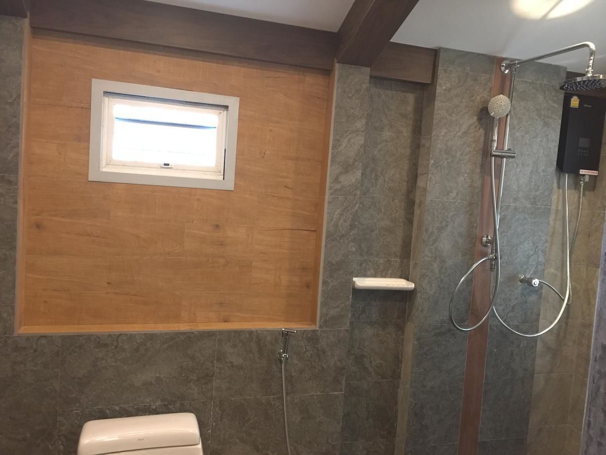 Un baño con tocador de madera, ducha con cabezal de ducha de mano y una ventana sobre el tocador.