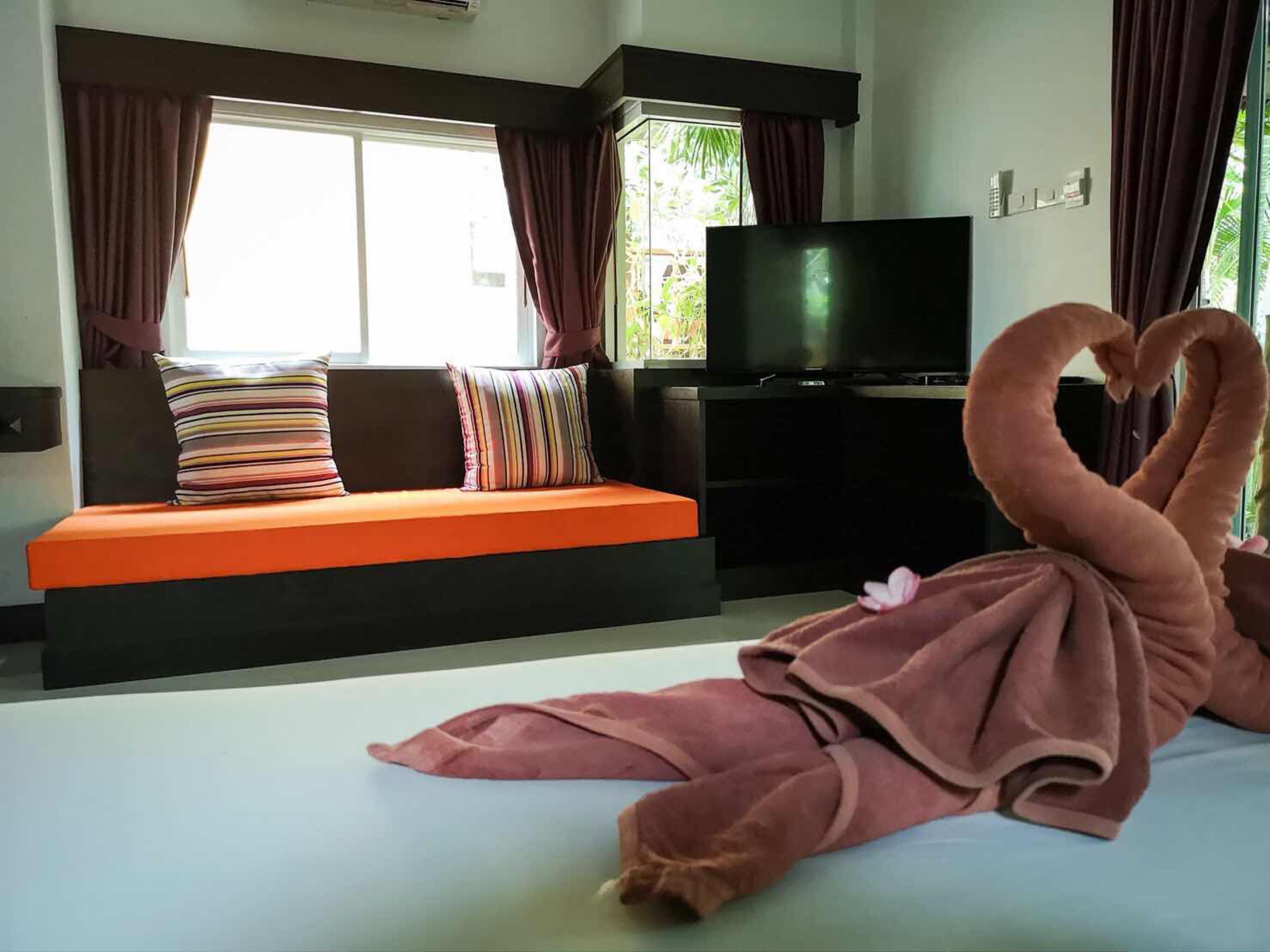 A hotel room with a sofa bed, a flat-screen TV, and a heart-shaped towel decoration.