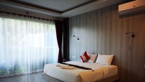 A modern bedroom with a large bed, a view of greenery through sheer curtains, and a wooden wall. - Vipa Tropical Resort (Krabi)