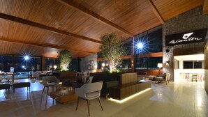 A spacious lobby with a wooden ceiling, a reception desk, seating areas, and large windows. - Hotel Village Le Canton (Teresópolis)