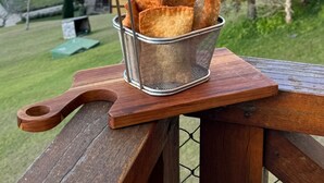 A basket of fried snacks on a wooden picnic table with a rural landscape in the background. - Hotel Village Le Canton (Teresópolis)