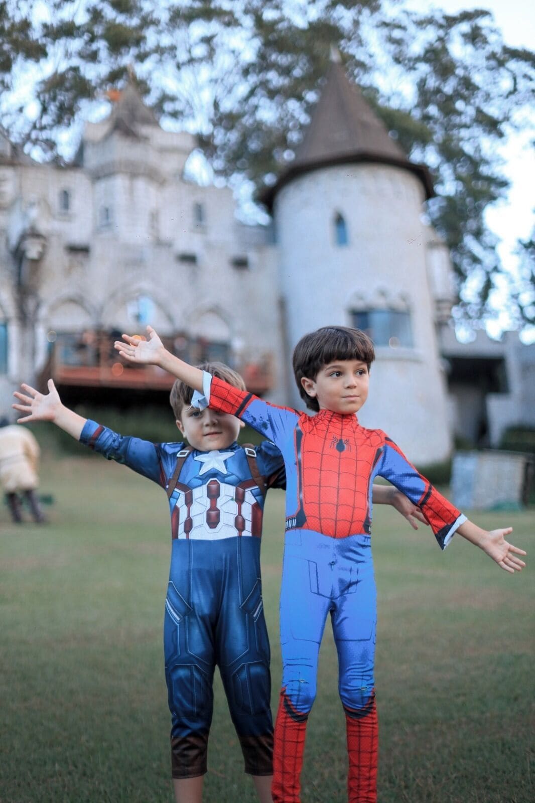 Two children in superhero costumes standing in front of a castle-like building.
