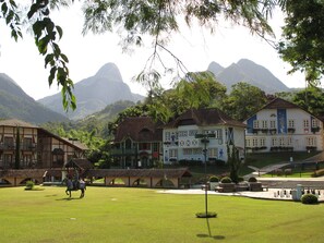 A traditional building with a balcony, surrounded by lush greenery and mountains in the background. - Hotel Village Le Canton (Teresópolis)