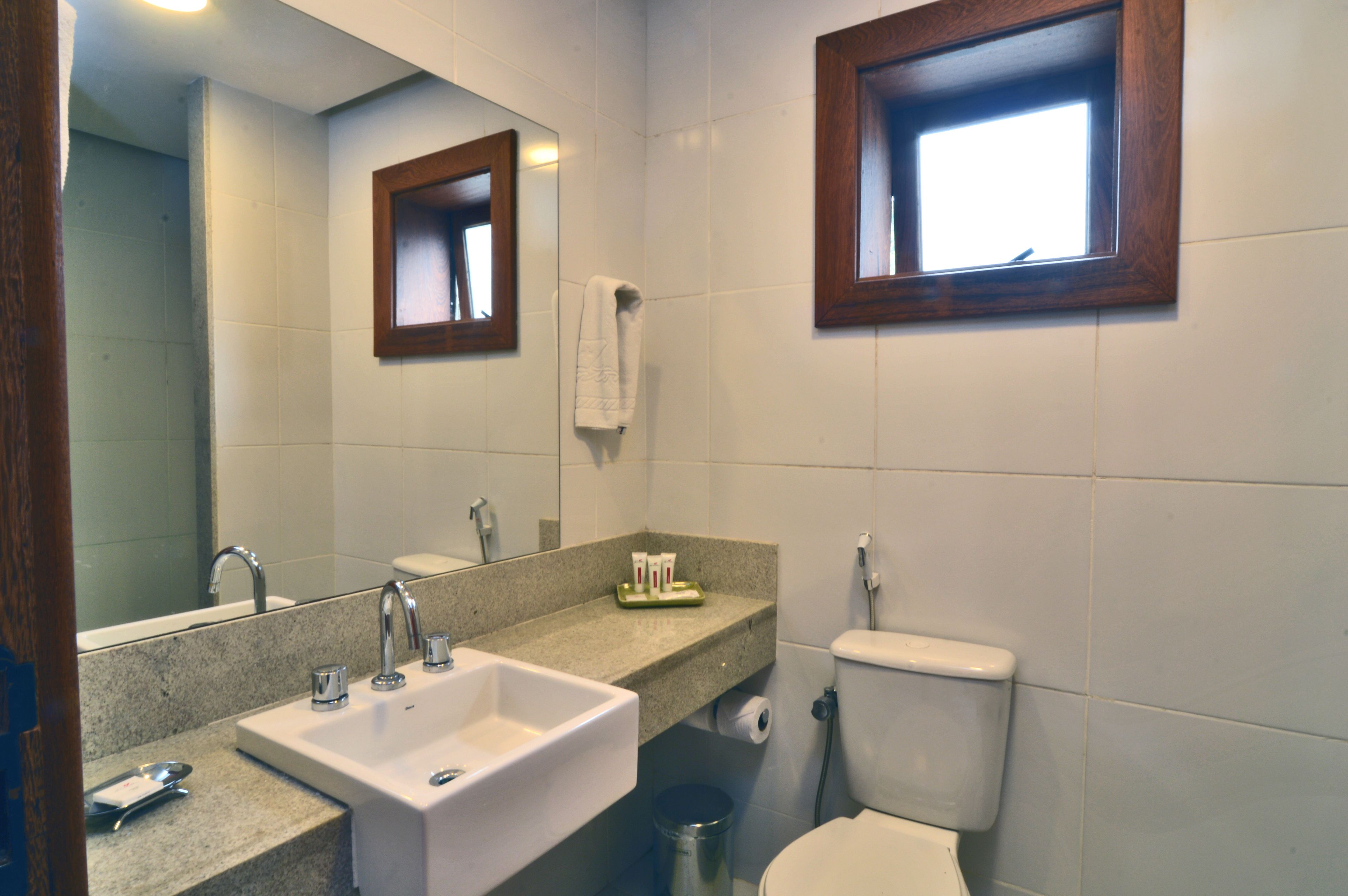A bathroom with a sink, mirror, toilet, and a window.