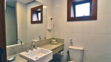 A bathroom with a sink, mirror, toilet, and a window.