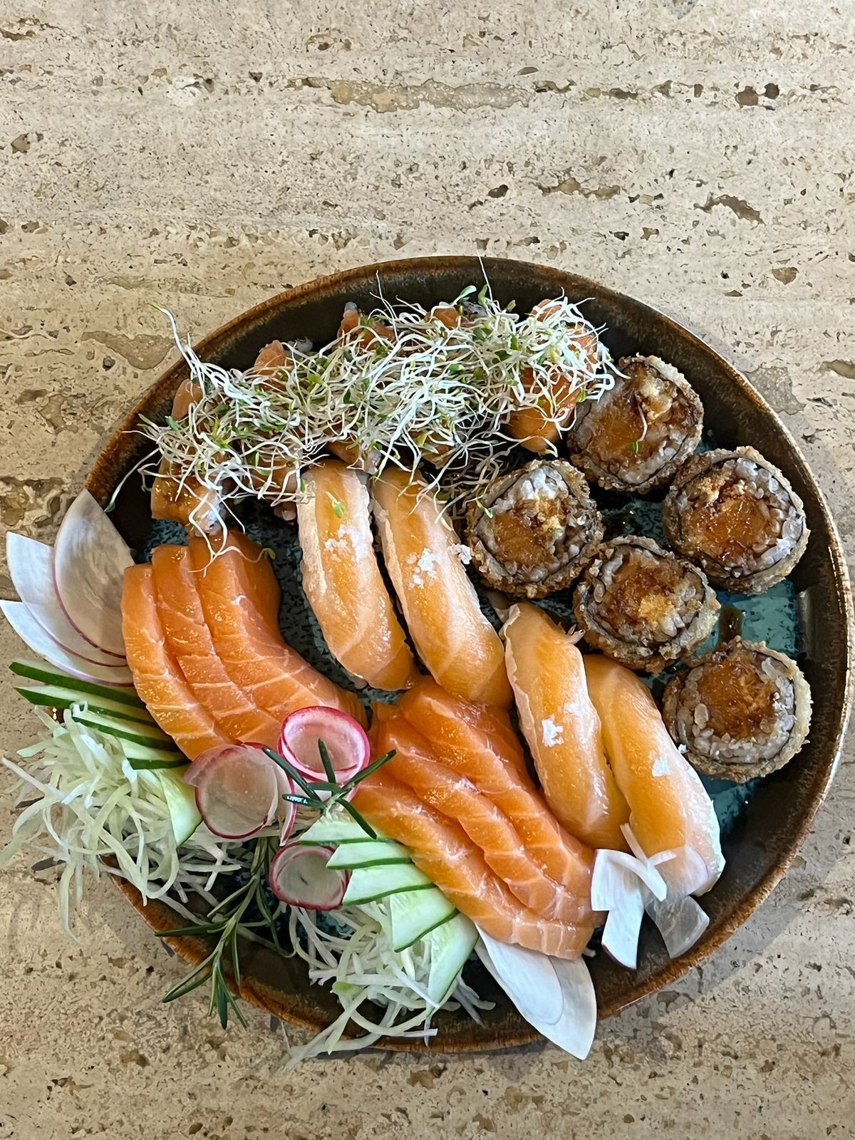 A plate of sushi with salmon, rolls, and garnishes.