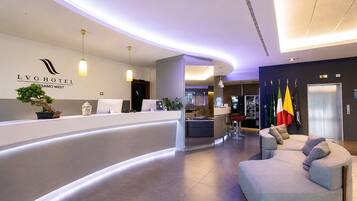 Ein Hotel-Empfangsbereich mit einer gebogenen Rezeption, einer Sitzecke mit einer Couch und einer Bar mit Flaggen.
