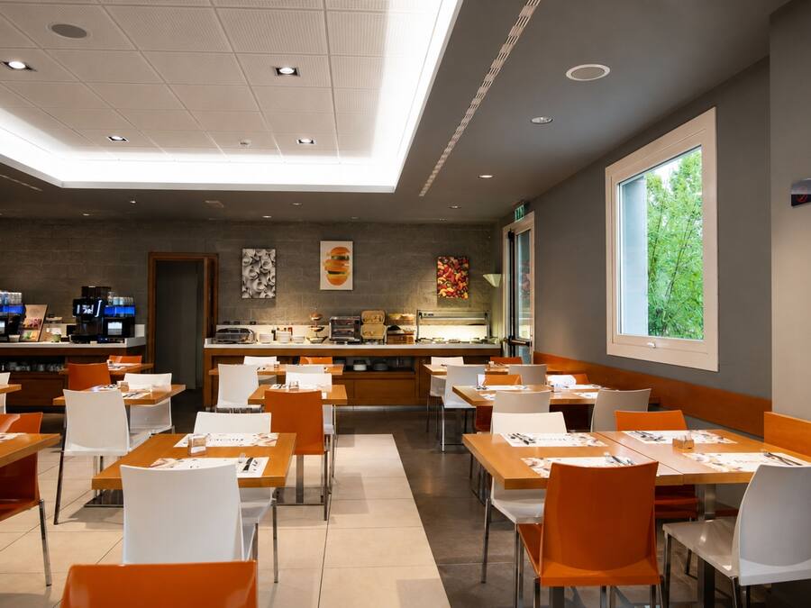 A modern restaurant interior with a long counter, multiple tables, and chairs.
