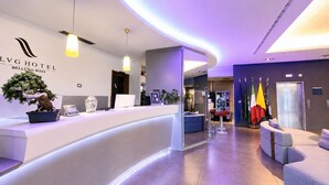 A hotel reception area with a curved counter, a bonsai tree, and flags. - LVG Hotel Collection - Bergamo West (Mozzo)