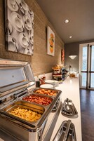 Montaje de bufé con diversos alimentos, un colgador de platos en la pared y una puerta que da al exterior.