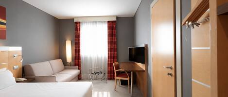 A hotel room with a bed, a desk with a chair, a TV, and a wardrobe.